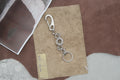 A silver metal keychain with a lobster clasp, decorative chain links, and a split key ring, displayed on a piece of brown paper over a textured brown and white surface.