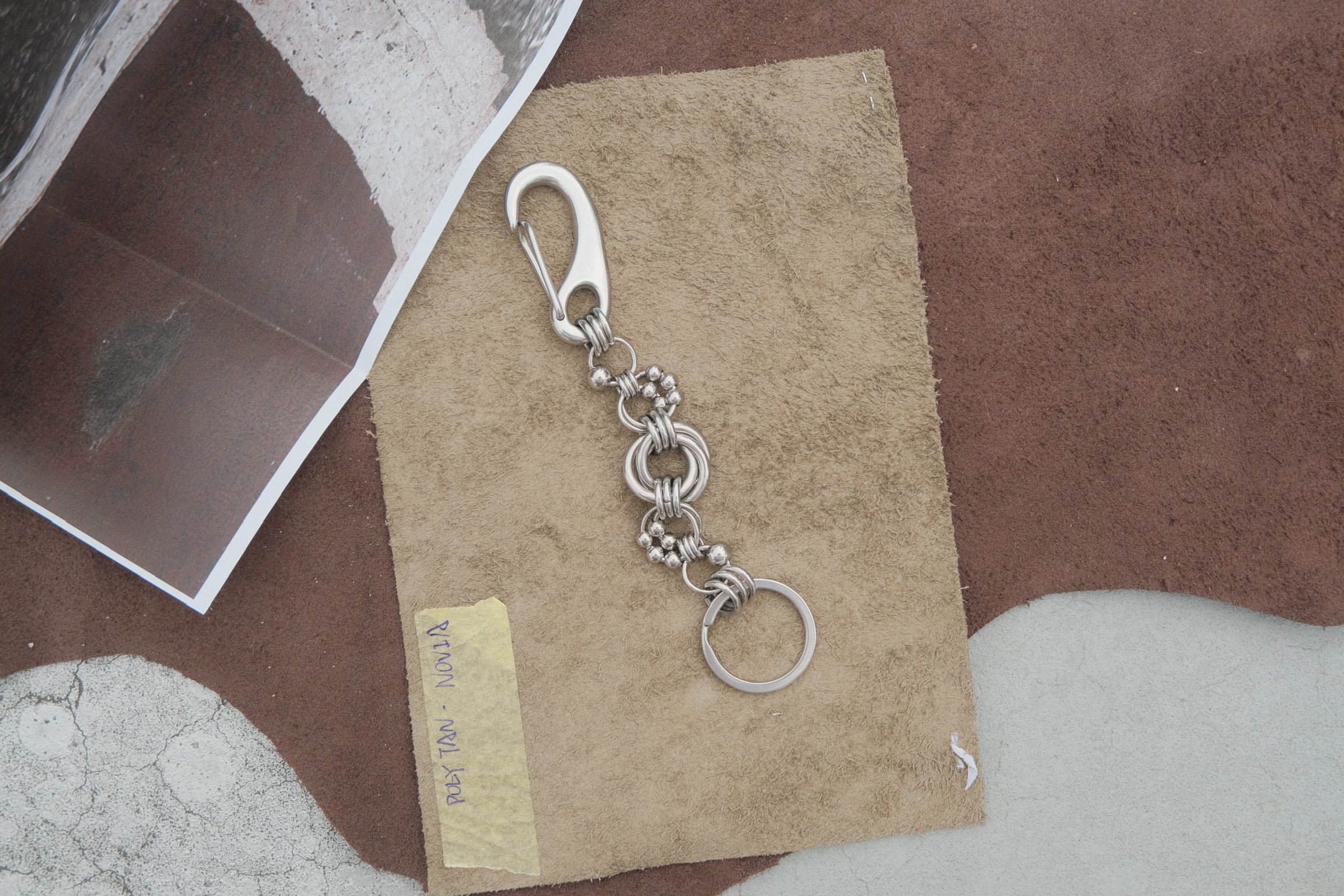 A silver metal keychain with a lobster clasp, decorative chain links, and a split key ring, displayed on a piece of brown paper over a textured brown and white surface.