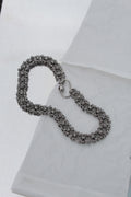 A silver-toned chainmail-style bracelet with a spring-ring clasp, displayed on a white textured surface.