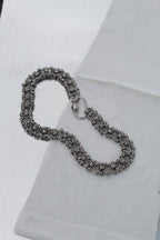 A silver-toned chainmail-style bracelet with a spring-ring clasp, displayed on a white textured surface.