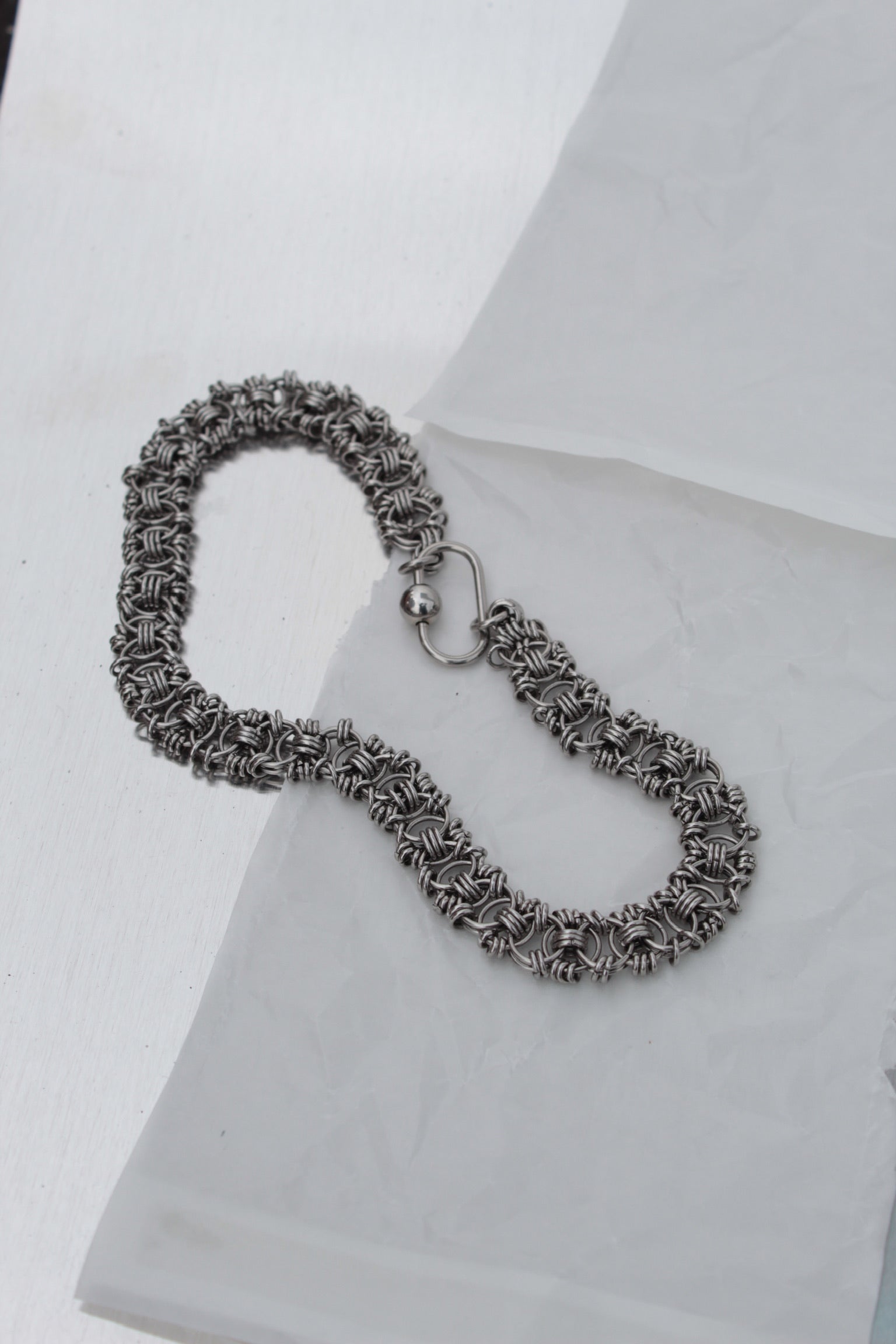 A silver-toned chainmail-style bracelet with a spring-ring clasp, displayed on a white textured surface.