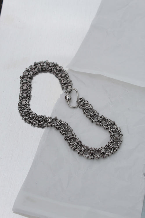 A silver-toned chainmail-style bracelet with a spring-ring clasp, displayed on a white textured surface.